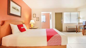 A hotel room with a bed, a desk, a chair, a lamp, and a framed picture on the wall.