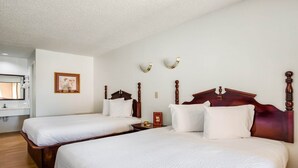 Ein Hotelzimmer mit zwei Betten, Holz-Kopfteilen, einem gerahmten Bild an der Wand und einem kleinen Nachttisch mit einer Lampe.