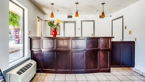 A reception desk with a large window, a red vase with flowers, and three pendant lights.