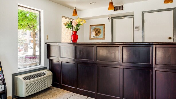 A reception area with a dark wooden counter, a red vase with flowers, a window with a tree view, and a wall-mounted picture.