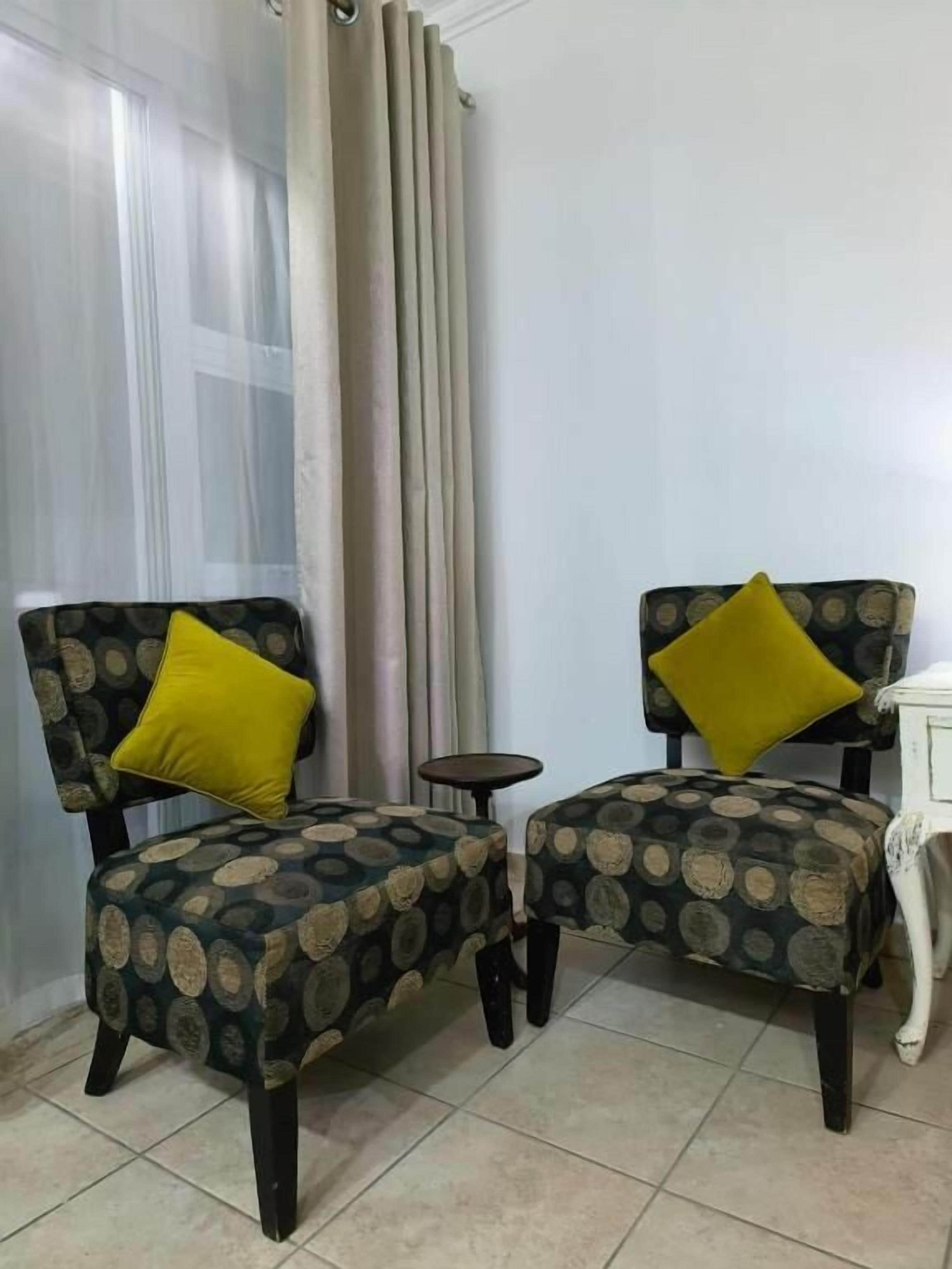 Quarto de canto com duas poltronas idênticas, uma mesinha redonda e um criado-mudo branco.