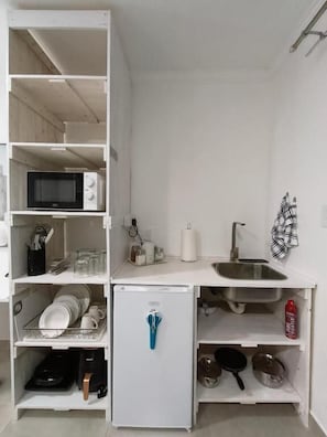 A compact kitchenette with a microwave, refrigerator, sink, and various kitchen utensils.