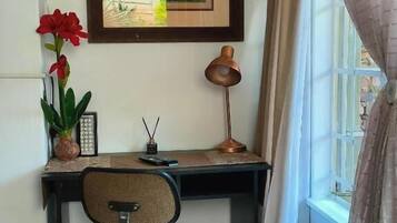 A corner office with a desk, chair, framed artwork, a potted plant, and a window with curtains.