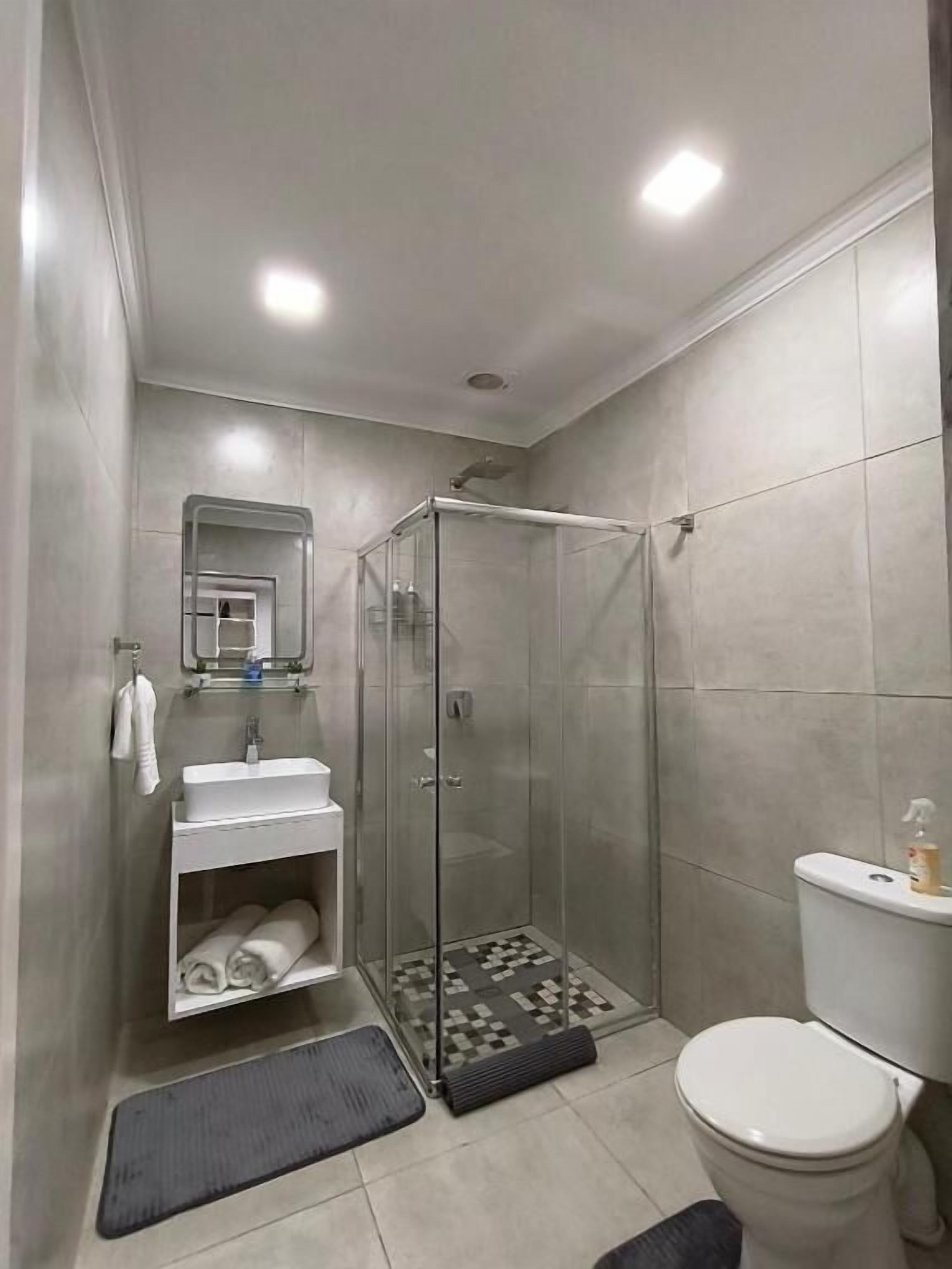 Uma casa de banho moderna com cabine de duche em vidro, sanita e lavatório com espelho.