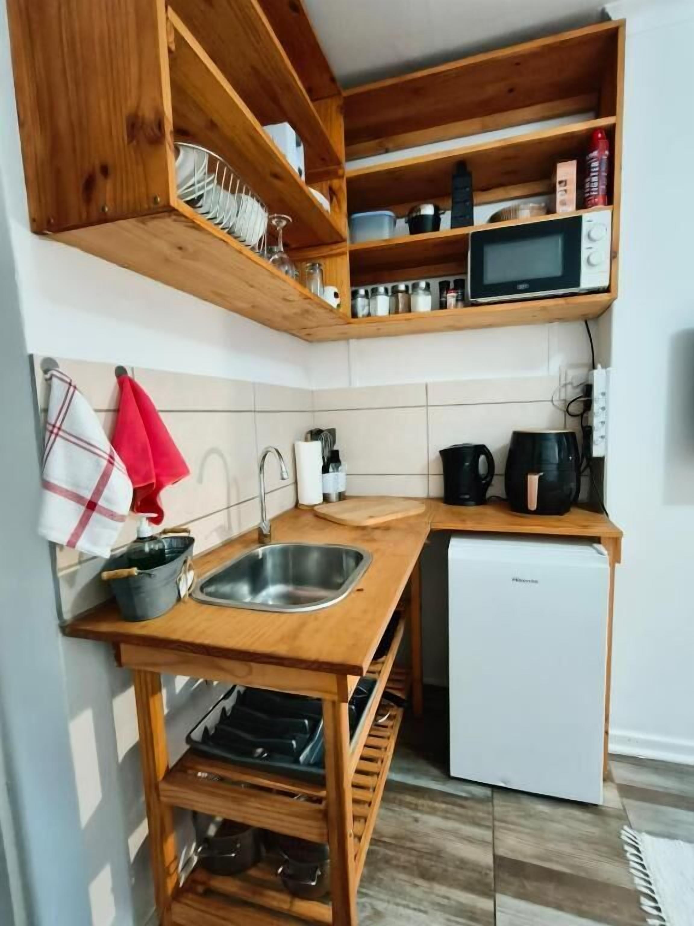 Uma cozinha compacta com prateleiras de madeira, micro-ondas embutido, pia e geladeira compacta.