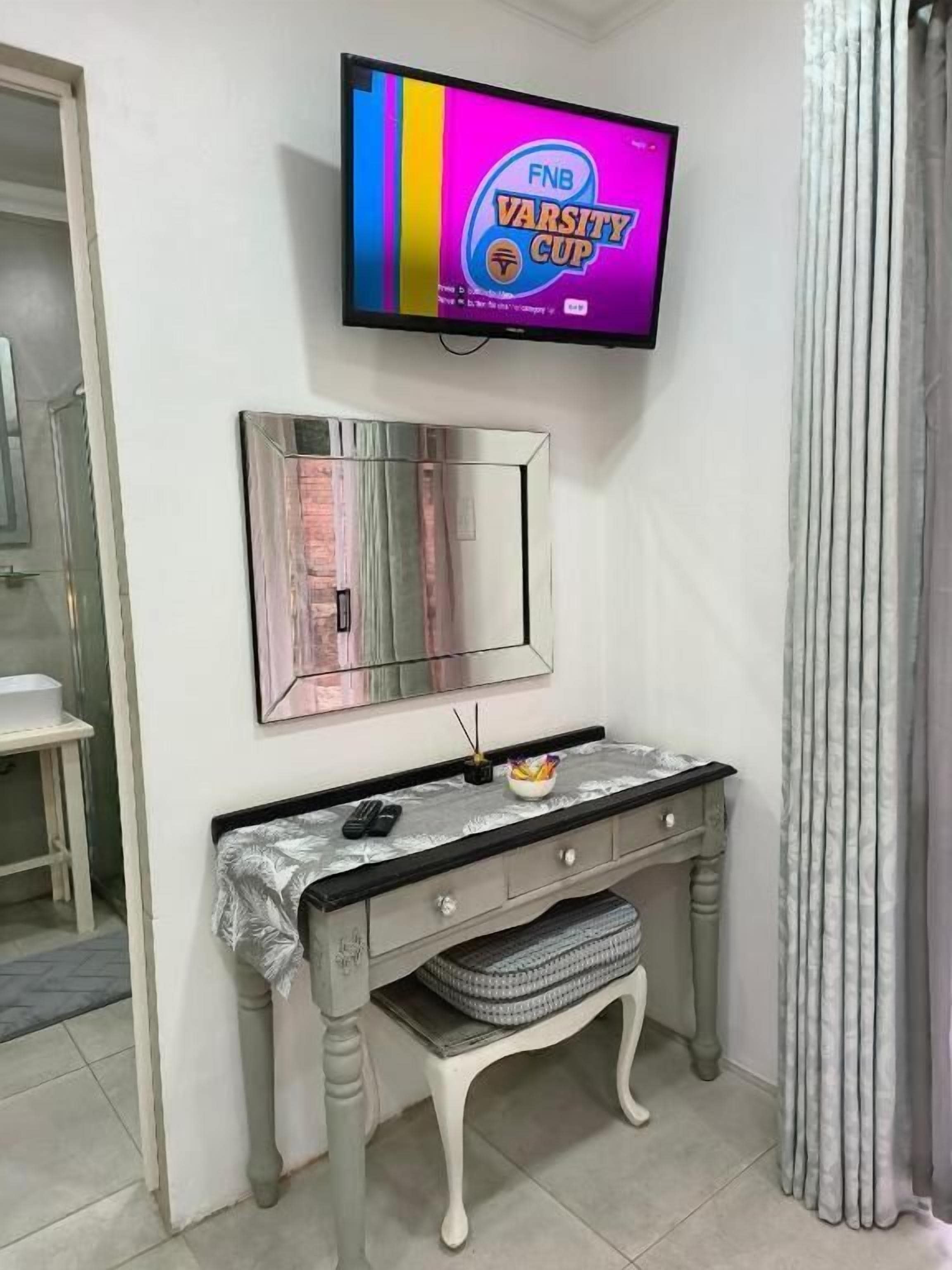 A room with a vanity, a television mounted on the wall, and a mirror above it.
