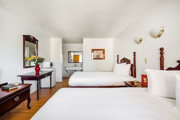 A hotel room with two beds, a desk, a mirror, and a small bathroom visible through an open door.