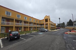 Un motel à plusieurs étages, avec une façade jaune, un parking et un drapeau.