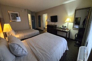 Habitación de hotel con dos camas, un escritorio, televisor y espejo.