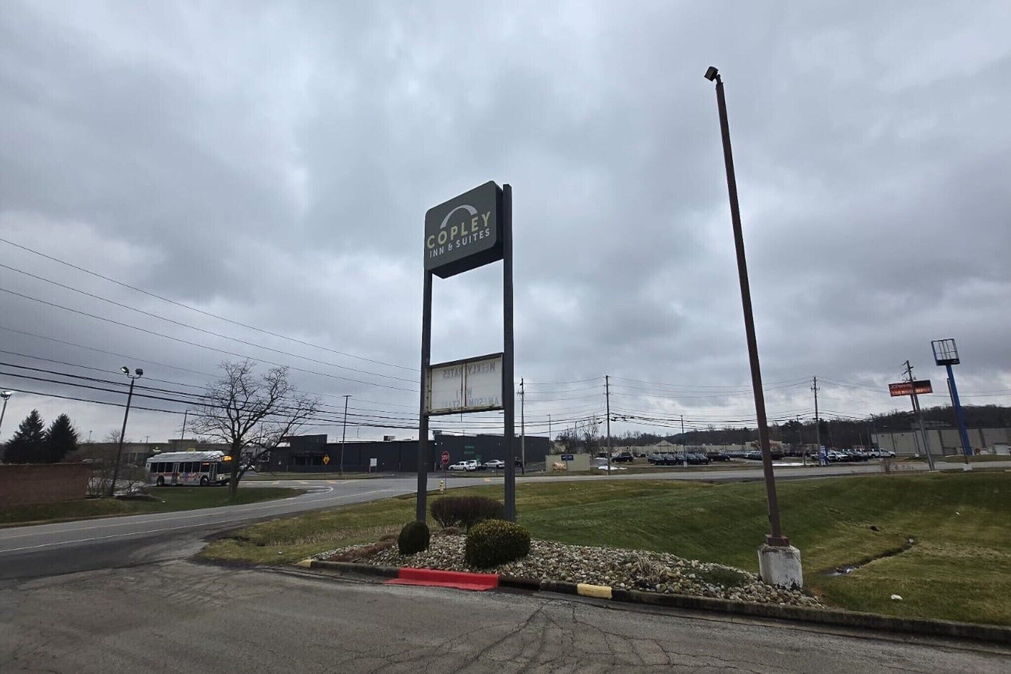 Letrero de Copley Inn & Suites en una zona comercial con estacionamiento y parada de autobús.