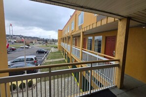 A multi-story yellow building with balconies, a parking lot, and a cloudy sky.