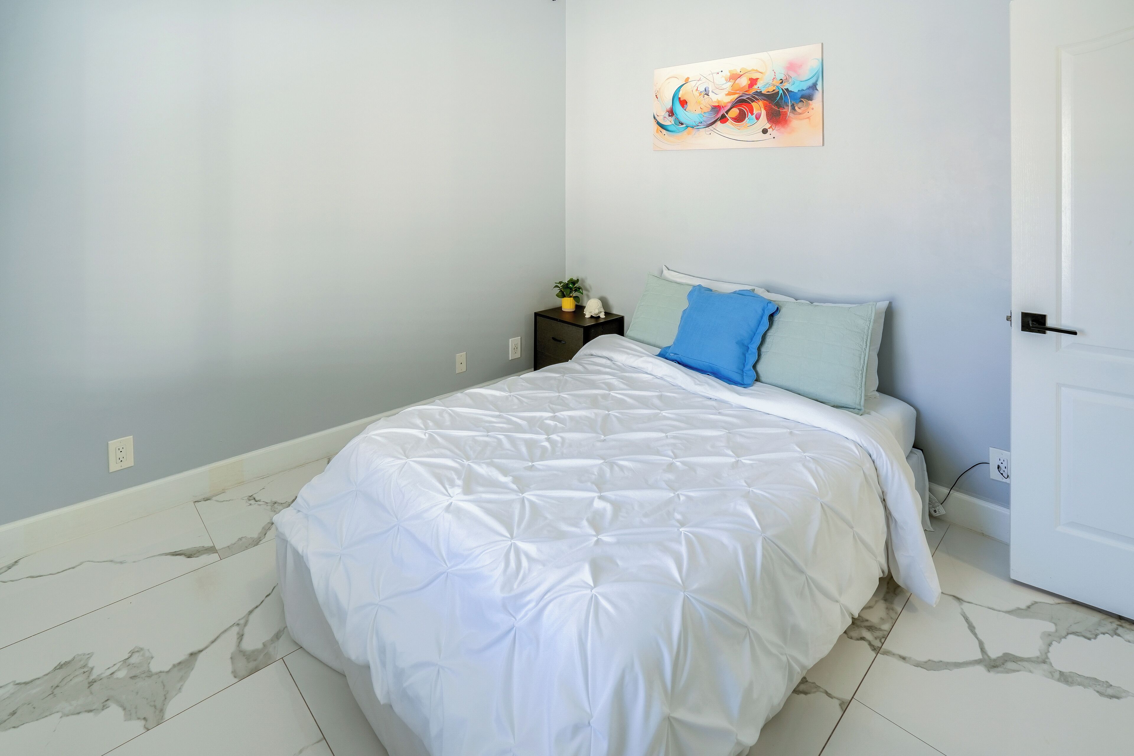 Ein Schlafzimmer mit Bett, Nachttisch, Wandbild und einer Tür.