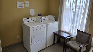 A laundry room with two washers and dryers, a small table, and a chair. There are signs indicating laundry room hours.
