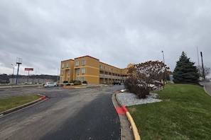 Ein mehrstöckiges Hotel mit gelber Fassade, einem Parkplatz und einer Rasenfläche mit einem kleinen Baum.