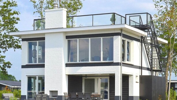 Une maison moderne à deux étages, dotée d’un toit plat, de grandes fenêtres et d’un balcon.