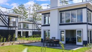 Une maison moderne à deux étages, dotée d’un toit plat, de grandes fenêtres et d’un espace extérieur aménagé pour se détendre.