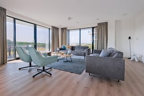 A spacious living room with a large window, a grey sofa, a light blue armchair, and a small coffee table. - Chic Dune View Stay in Breskens (Breskens)