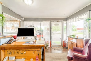 Una habitación con escritorio, computadora, silla y ventanas amplias.