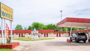 Motel Holiday Capri con fachada roja y blanca, un pequeño pabellón y un estacionamiento.