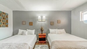 Una habitación con dos camas, una mesita de noche con lámpara e iluminación en la pared.