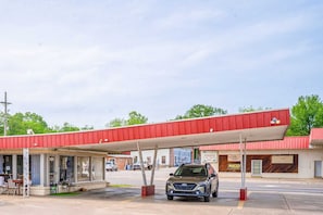 Una estación de servicio con toldo rojo, un coche aparcado debajo y una pequeña zona de estar al aire libre.