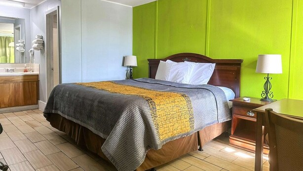 A hotel room with a bed, bedside lamps, a wooden nightstand, a desk, and a bathroom with a sink and mirror.