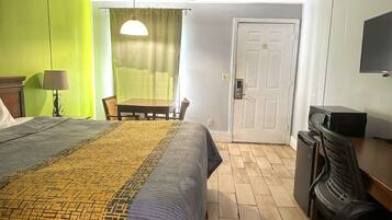 Une chambre d’hôtel avec un lit, un bureau, une chaise, une télévision et une porte.