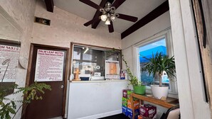 A Palm Leaf Motel reception area with a ceiling fan, a window with a view, a reception desk, and a door.