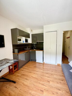 A compact kitchen with a microwave, toaster, and refrigerator, a small dining table, and a sofa in a living area.