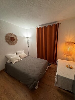 A bedroom with a bed, a bedside table with a lamp, a round wall decoration, and a curtain.