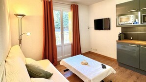 A compact room with a sofa, a small table, a TV, and a kitchenette. - STUDIO LA FOUX D'ALLOS (Allos)