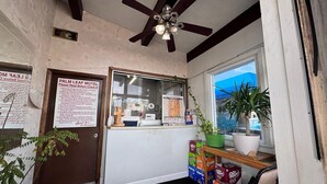 A Palm Leaf Motel reception area with a ceiling fan, a window with a view, a reception desk, and a door with a sign. - 3 Full Beds Non-Smoking (Ashland, VA)