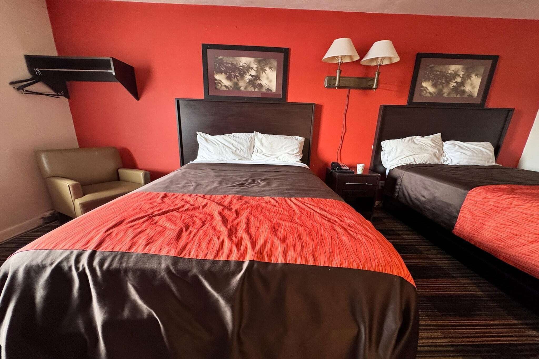 A hotel room with two beds, a chair, and two wall-mounted lamps.