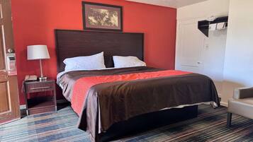 Una habitación de hotel con cama, una mesita de noche con lámpara, una silla y una puerta.