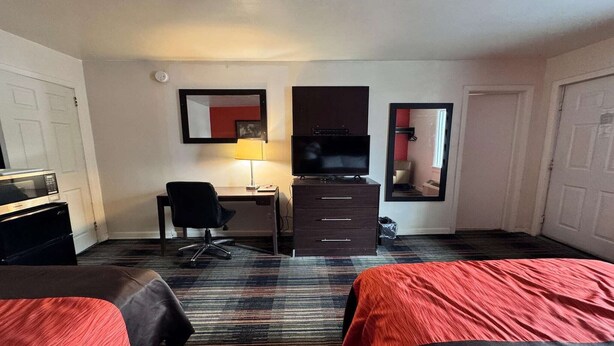 Een hotelkamer met twee bedden, een bureau met stoel, een televisie, een dressoir en een spiegel.