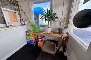 Una habitación pequeña con ventana, un escritorio con planta en maceta, una silla y varias cajas de aperitivos.
