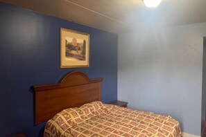 A bedroom with a wooden headboard, a patterned bedspread, a framed picture on the wall, and a nightstand. - King Bed|Smoking|Chicago (Chicago IL)