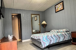 A bedroom with a bed, a wooden dresser, a mirror, and a lamp.