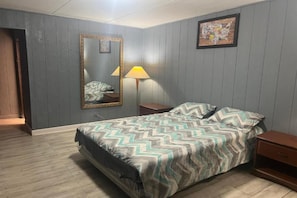 A bedroom with a bed, a nightstand, a lamp, a mirror, and a wall map.