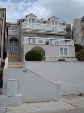 A two-story residential building with a balcony, a staircase, and a small garden area. - Apartman Nada (Cavtat)