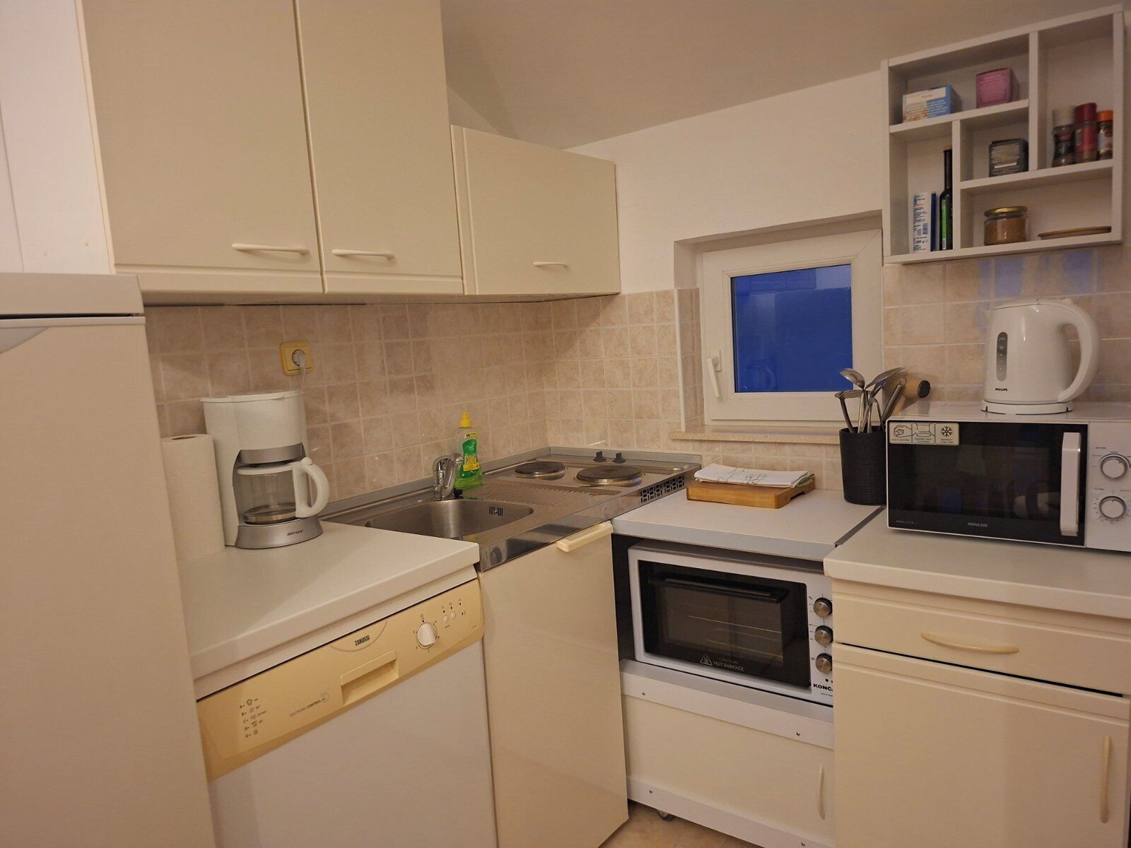 A compact kitchen with a coffee maker, microwave, oven, and a window with a view.