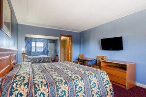 A bedroom with a large bed, a desk, a chair, a television, and a window with curtains.