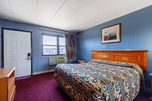 A hotel room with a patterned bedspread, a wooden headboard, a window with curtains, a door, and a framed picture on the wall.
