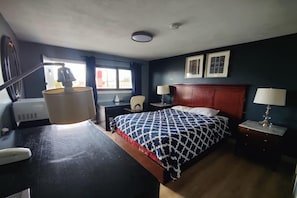 Ein Hotelzimmer mit Bett, Nachttischen, einem Schreibtisch, einem Sessel, einem Fenster mit Vorhängen und einer Deckenleuchte.