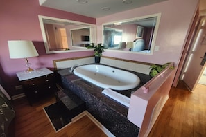 A bathroom with a bathtub, a vanity with a mirror, a potted plant, and a towel rack. - King Bed Non-Smoking (Chicago)