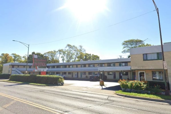 A motel with a signboard, a parking lot, and a building with a flat roof. - King Bed Non-Smoking (Chicago)