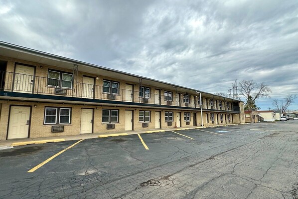 Un motel à étages, avec une rangée de chambres, un parking et un ciel dégagé.