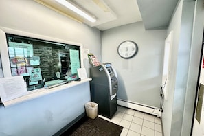 Zona de recepción con mostrador, reloj, cajero automático y contenedor de basura.