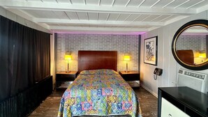 Una camera d'albergo con una testiera a motivi a mattoni, due lampade da comodino, uno specchio rotondo e una TV a schermo piatto.