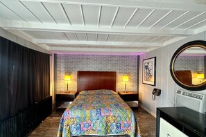 A hotel room with a brick-patterned headboard, two bedside lamps, a round mirror, and a flat-screen TV.